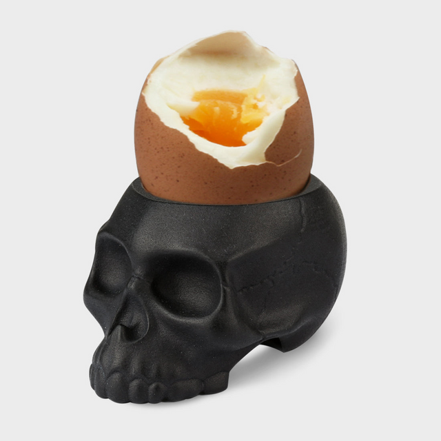 Black skull-shaped egg holder with a cracked brown egg on a light gray background